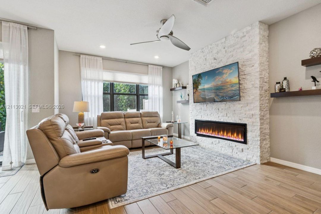 Living area featuring a floor-to-ceiling white stone fireplace surround, modern linear electric fireplace, wood-finish flooring, recessed lighting, and floating wall shelves