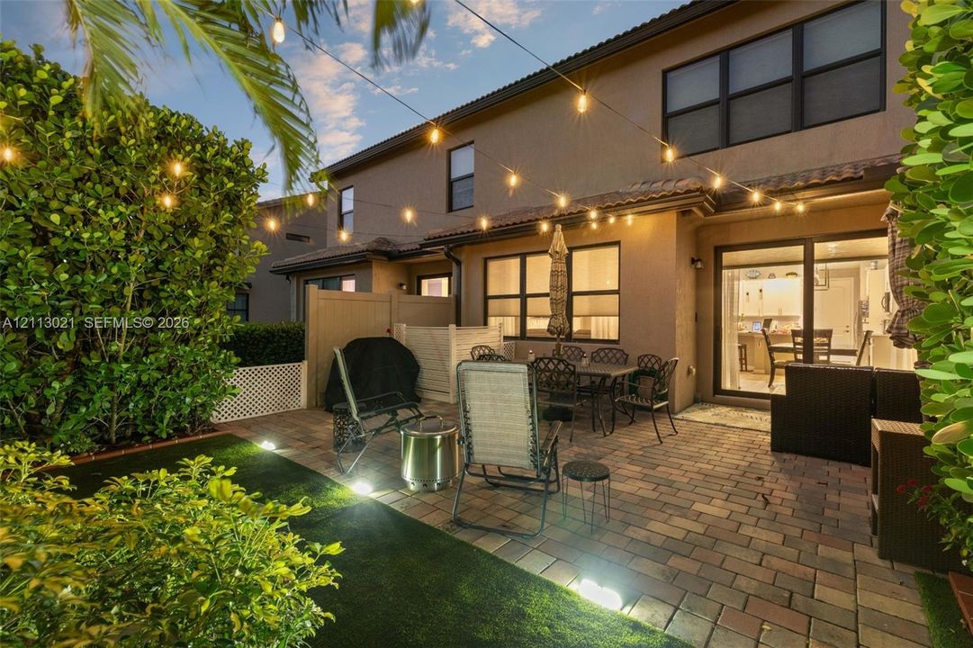 Paver patio featuring integrated landscape lighting, artificial turf, and privacy fencing