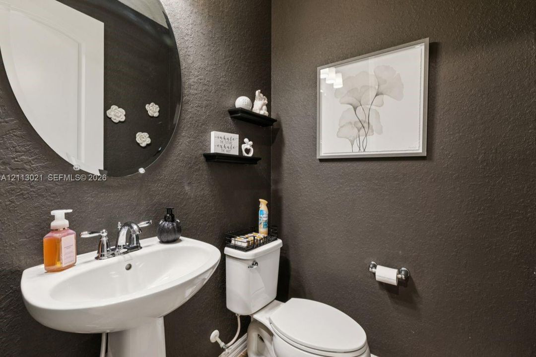 Oval wall-mounted mirror, white ceramic pedestal sink, chrome finish faucet, two built-in floating shelves, and textured dark-toned walls