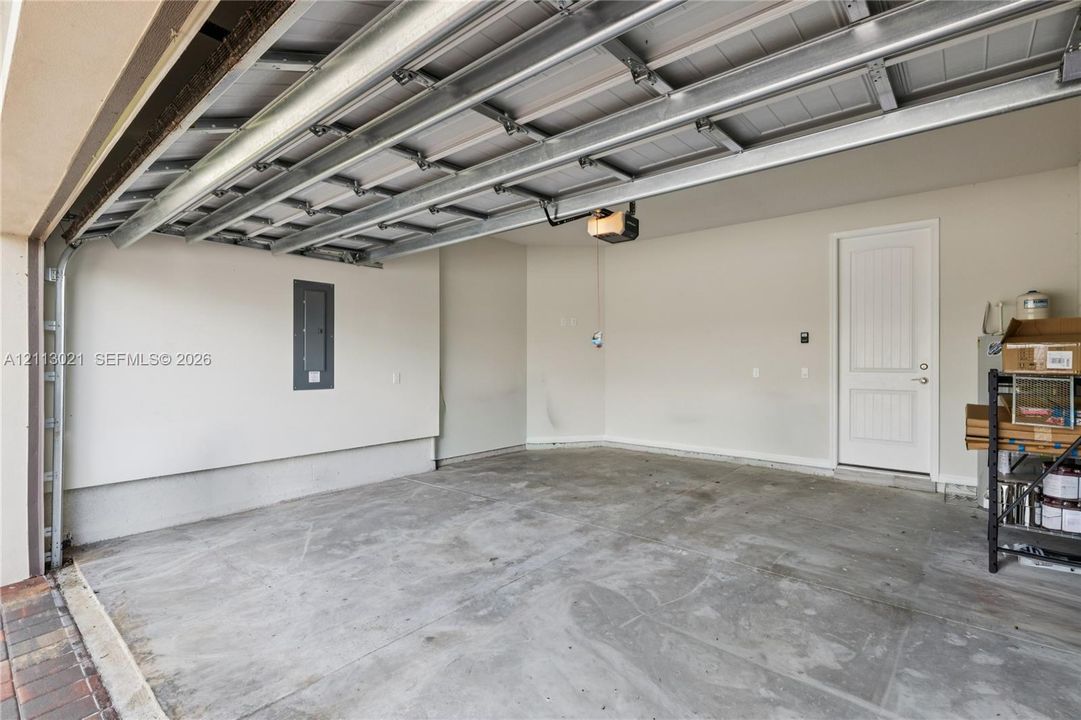 Finished garage featuring concrete flooring, a panel door, exposed ceiling joists, and an electrical service panel