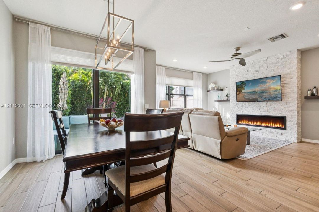 Open-concept interior featuring wood-finish flooring, a textured stone accent wall with a linear electric fireplace, and a geometric metal pendant light