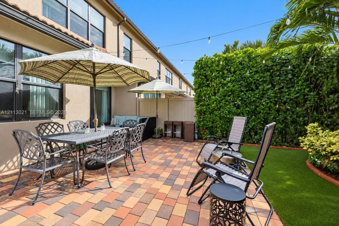 Paver patio featuring integrated string lighting, synthetic turf lawn, and perimeter privacy hedges