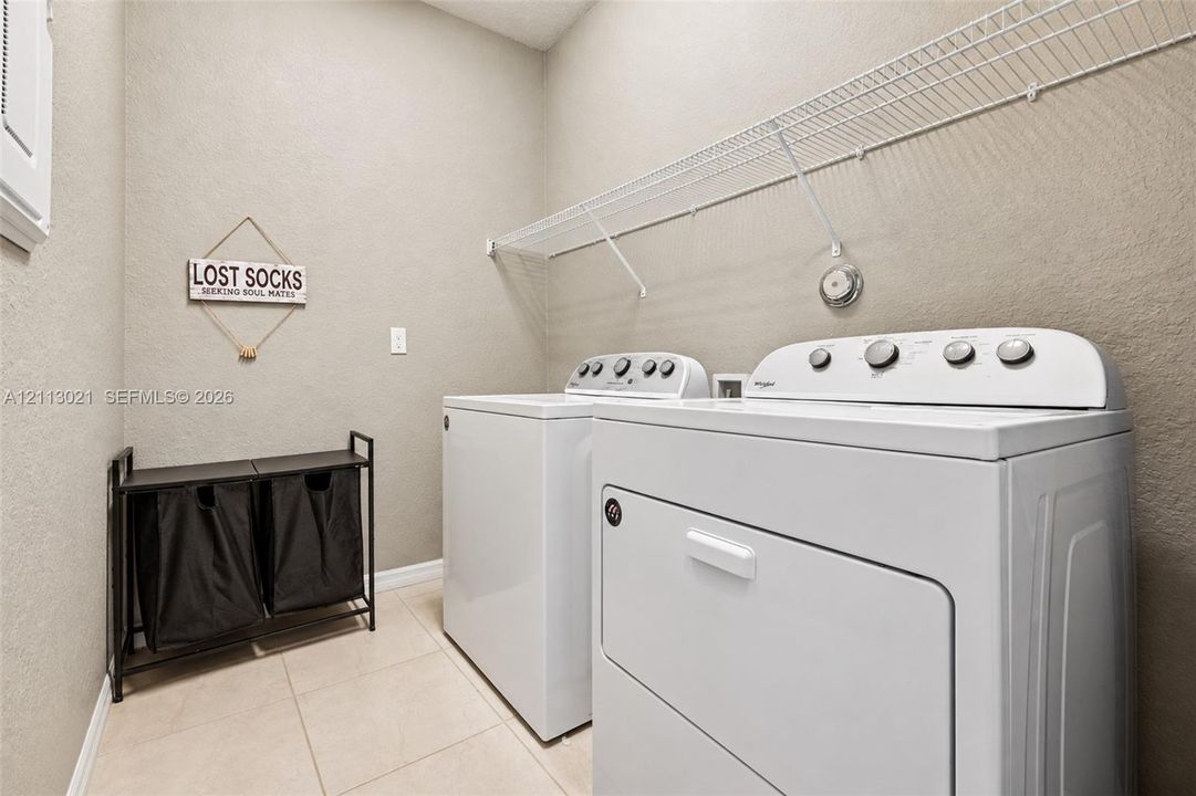 Laundry area featuring neutral-toned tile flooring, textured wall finishes, and integrated white wire shelving