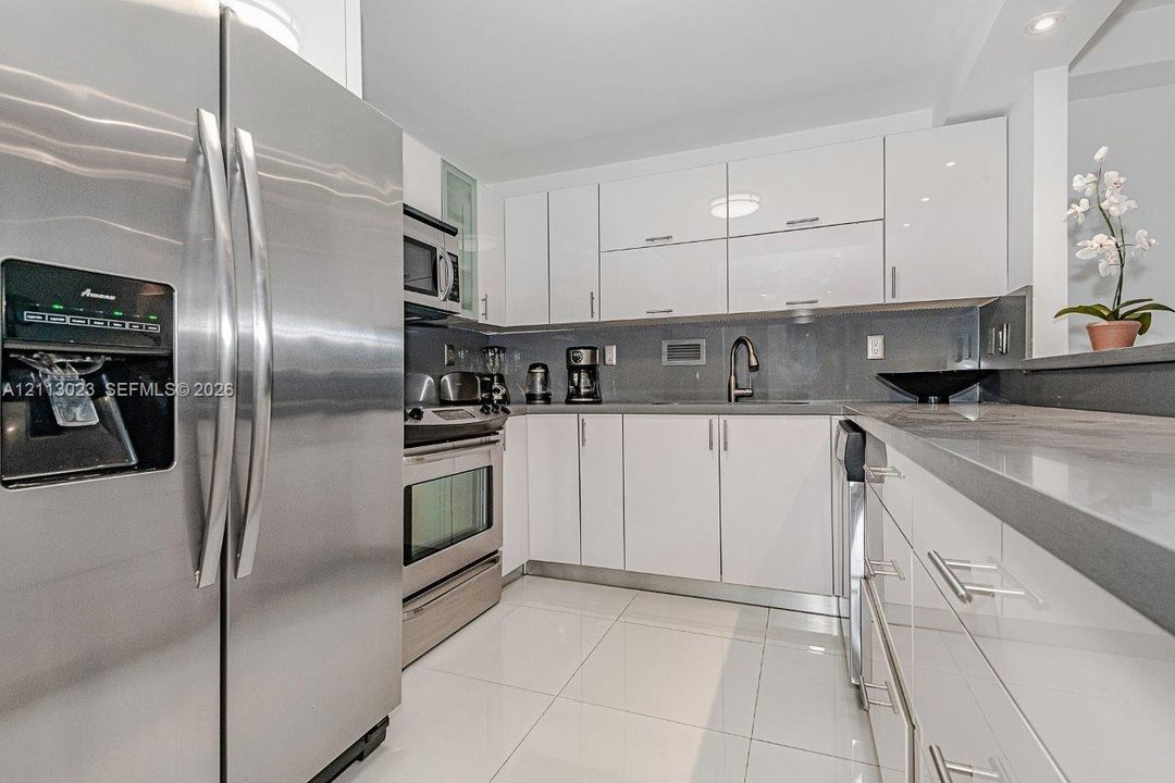 Kitchen featuring high-gloss white cabinetry, stainless steel appliances, solid-surface countertops, a gooseneck faucet, and white tile flooring