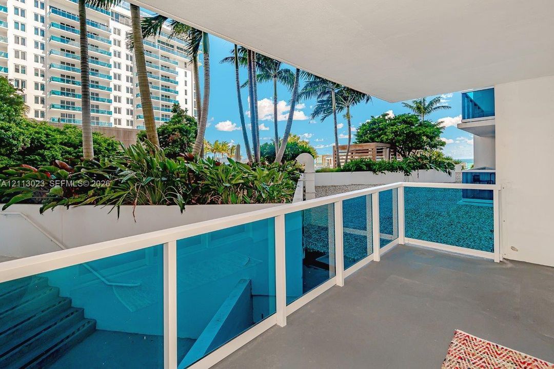 Covered balcony with white railings and blue-tinted glass panels, featuring exterior landscaping with palm trees