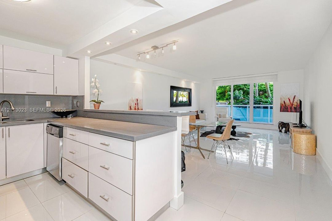 Kitchen featuring glossy white flat-panel cabinetry, solid-surface countertops, stainless steel undermount sink, and recessed lighting, complemented by polished tile flooring