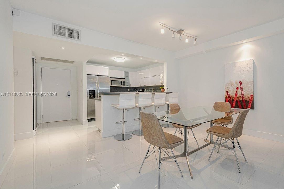 Open-concept kitchen featuring high-gloss cabinetry, stainless steel appliances, a breakfast bar, and polished white tile flooring