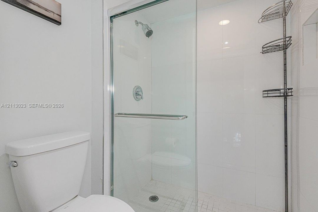 Glass-enclosed shower with white wall tile, mosaic tile shower floor, and chrome fixtures