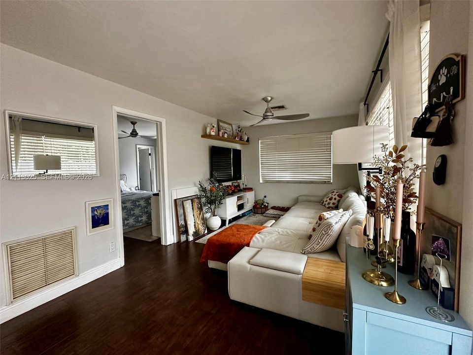Living area featuring wood-finish flooring, a ceiling fan, horizontal blinds, and a built-in wall shelf