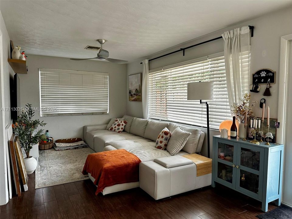 Living area featuring wood-finish flooring, a ceiling fan, and large windows with horizontal blinds