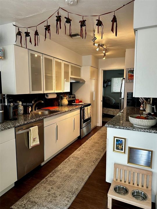 Kitchen featuring white cabinetry with frosted glass inserts, speckled stone countertops, stainless steel appliances, and dark wood-finish flooring