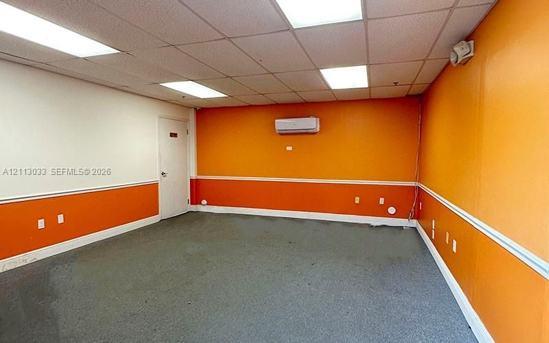Interior space featuring a drop ceiling with recessed panel lighting, wall-mounted ductless air conditioning unit, and carpeting