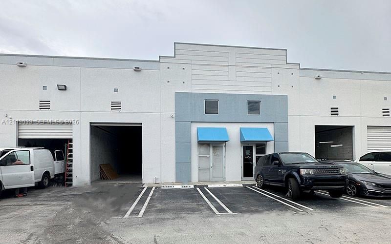 Commercial building featuring a concrete facade, dual roll-up bay doors, individual glass-entry storefronts with metal awnings, and dedicated asphalt parking