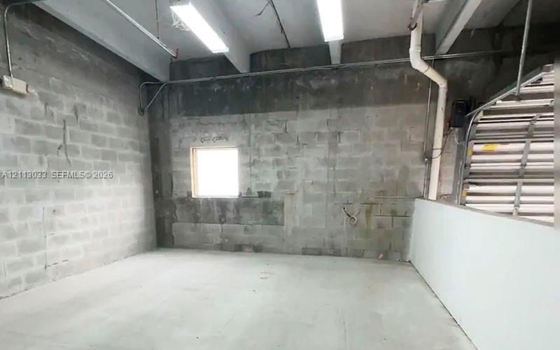 Industrial space featuring concrete masonry unit walls, a concrete floor, suspended linear lighting, and a square window