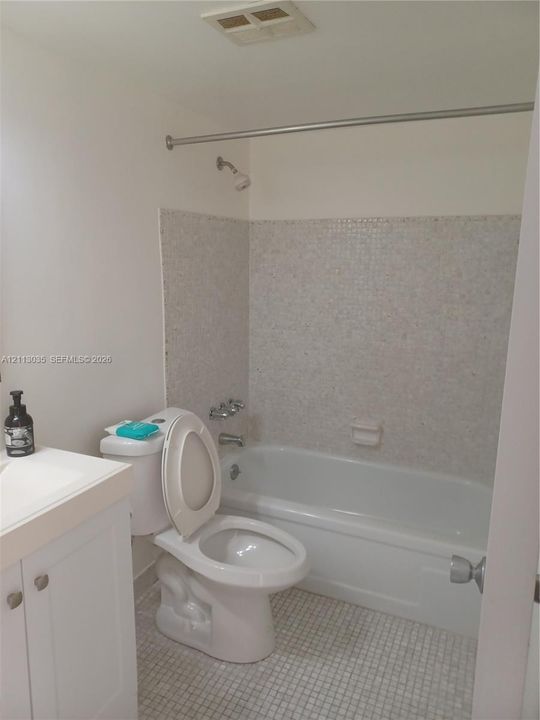 Bathroom featuring a white vanity cabinet, a shower-tub combination with mosaic tile surround, and mosaic tile flooring