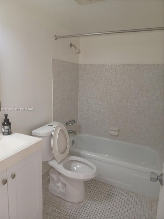 Bathroom featuring a white vanity cabinet with a solid-surface countertop, a tub-shower combination with mosaic tile wall surround, and small-format tile flooring