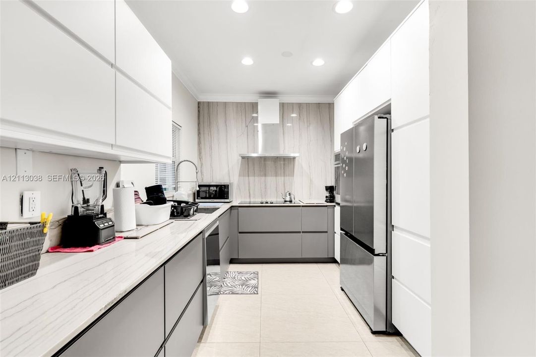 Contemporary kitchen featuring flat-panel cabinetry, stone-finish countertops, full-height decorative backsplash, stainless steel range hood, and tile flooring
