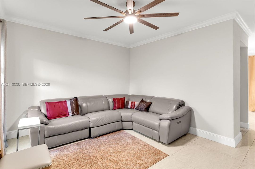 Interior space featuring neutral wall paint, multi-blade ceiling fan with integrated lighting, crown molding, and large-format tile flooring