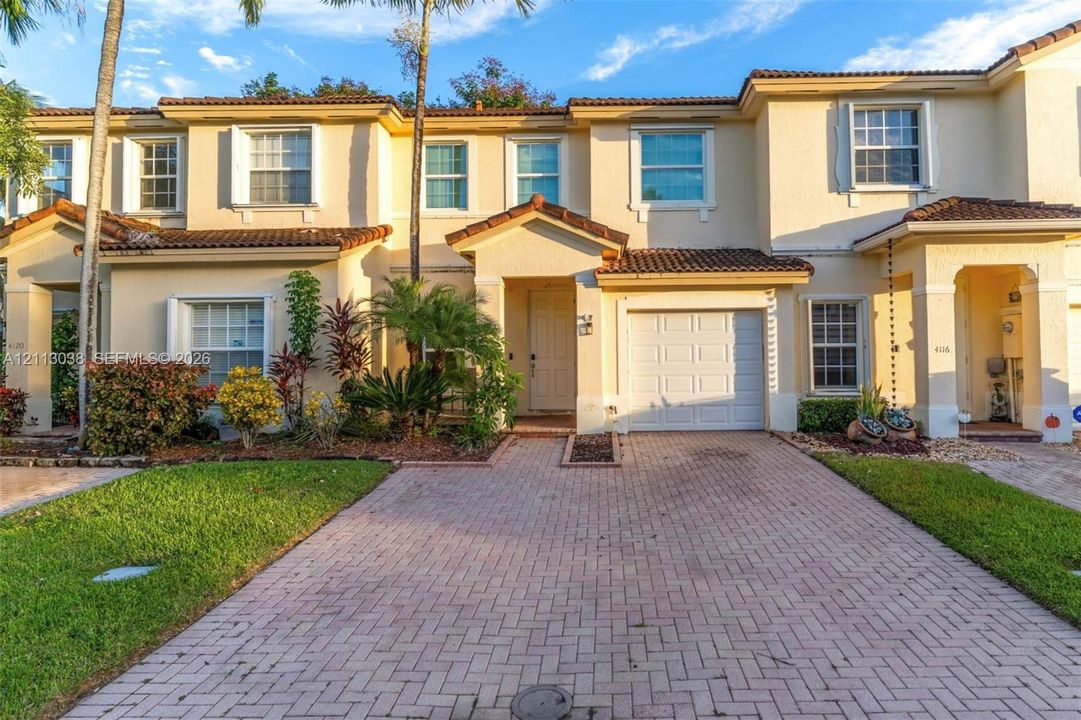 Two-story stucco exterior featuring a tile roof, brick-paver driveway, and an attached one-car garage