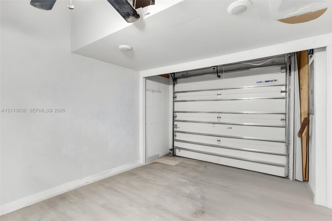 Enclosed garage space featuring a paneled sectional garage door, recessed lighting, and wood-finish flooring