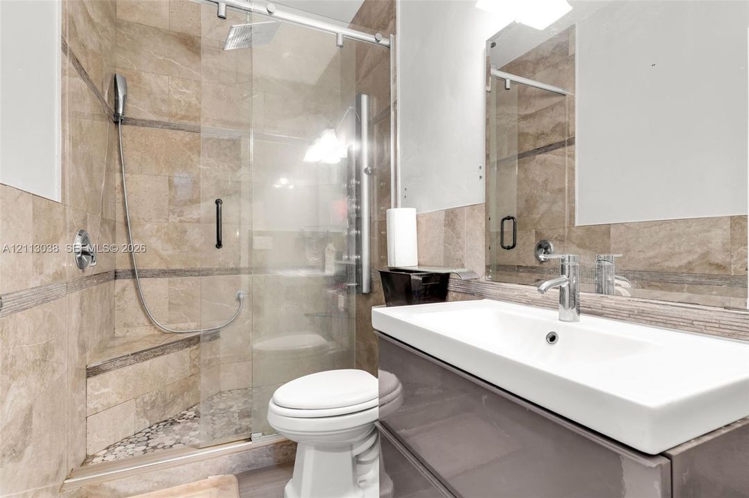 Walk-in glass shower enclosure featuring tiled walls, a built-in bench, and a handheld shower fixture, complemented by a wall-mounted floating vanity with an integrated sink and polished chrome faucet