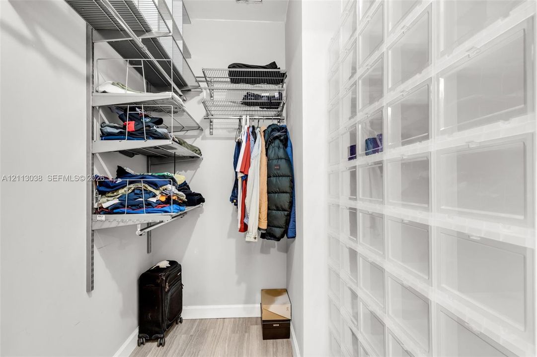 Storage area featuring wall-mounted metal shelving, a hanging rod, and integrated grid-style wall compartments, complemented by wood-finish flooring