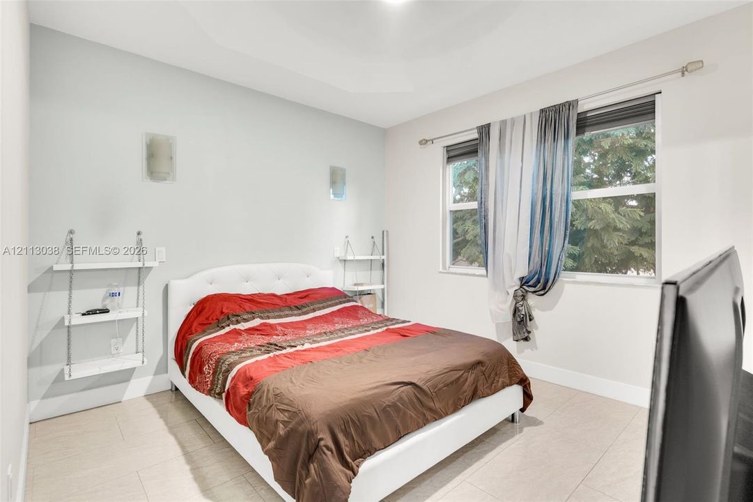 Neutral-toned interior featuring a tray ceiling, large-format tile flooring, wall-mounted light fixtures, and windows with integrated hardware