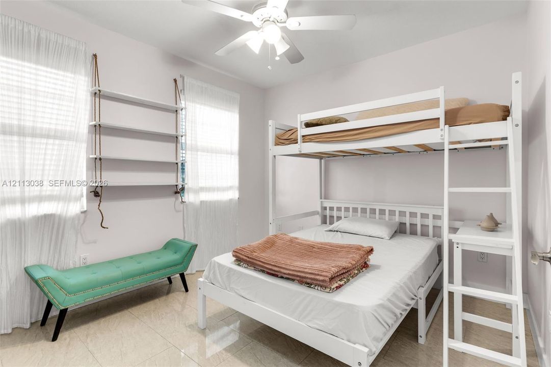 Interior space featuring neutral wall tones, large-format tile flooring, white-finish ceiling fan with integrated lighting, and wall-mounted white shelving units with rope detailing