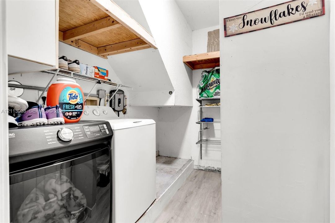 Laundry area featuring wood-finish flooring, built-in wooden shelving, and metal wire rack storage