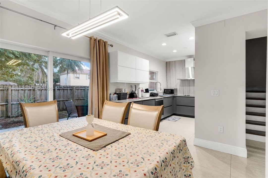 Modern kitchen featuring handleless cabinetry, stone-finish countertops, stainless steel wall-mounted range hood, and large-format tile flooring
