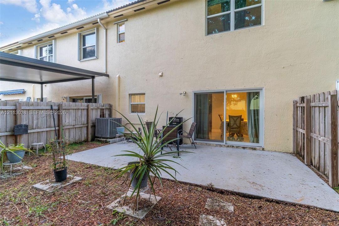 Rear exterior featuring a concrete patio, covered metal awning, and wood privacy fencing
