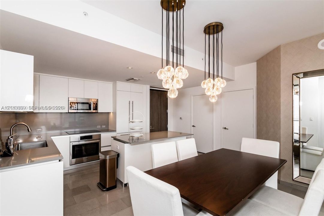 Contemporary kitchen featuring white flat-panel cabinetry, stainless steel appliances, a flush-mount electric cooktop, quartz countertops, and dual multi-bulb pendant light fixtures