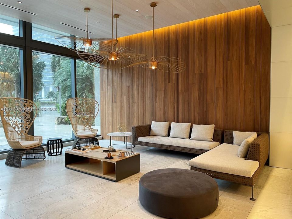 Floor-to-ceiling glass windows, wood-paneled accent wall, recessed perimeter lighting, large-format tile flooring, and metallic architectural pendant fixtures