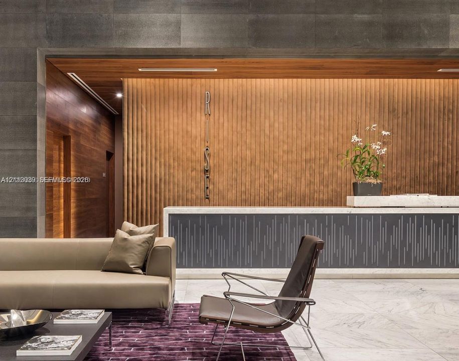 Reception area featuring large-format dark stone wall cladding, vertical wood-slat paneling, stone flooring, and a bespoke reception desk with integrated lighting