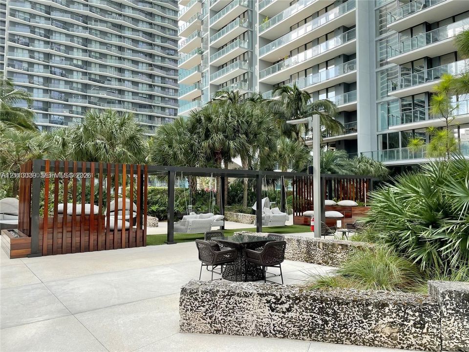 Outdoor terrace featuring large-format concrete pavers, custom dark wood-slatted privacy screens, a natural stone retaining wall, and integrated metal pergola structures