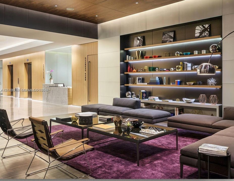 Lobby featuring a wood-panel ceiling, built-in recessed shelving with integrated lighting, polished stone flooring, and flush-mounted wall paneling