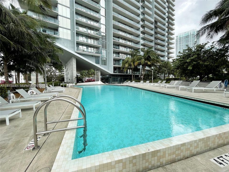 In-ground swimming pool featuring a tiled waterline, metal handrails, and surrounding stone deck