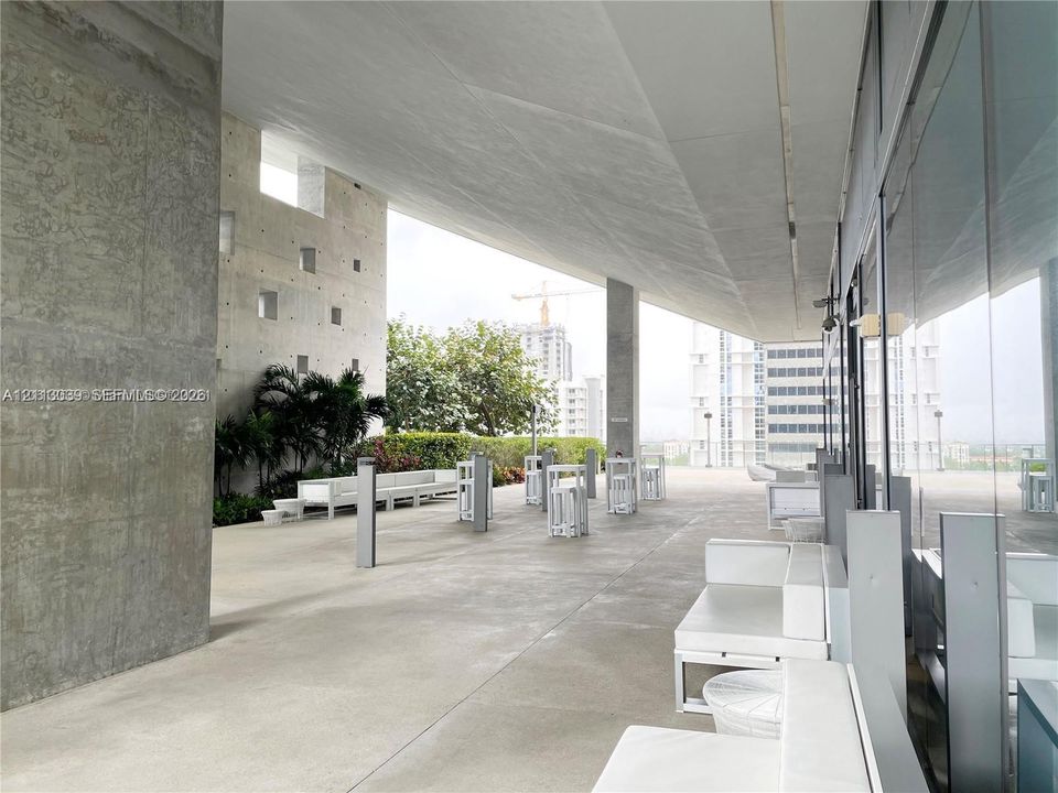 Expansive covered terrace featuring exposed concrete structural elements, floor-to-ceiling glass paneling, and integrated landscape planters