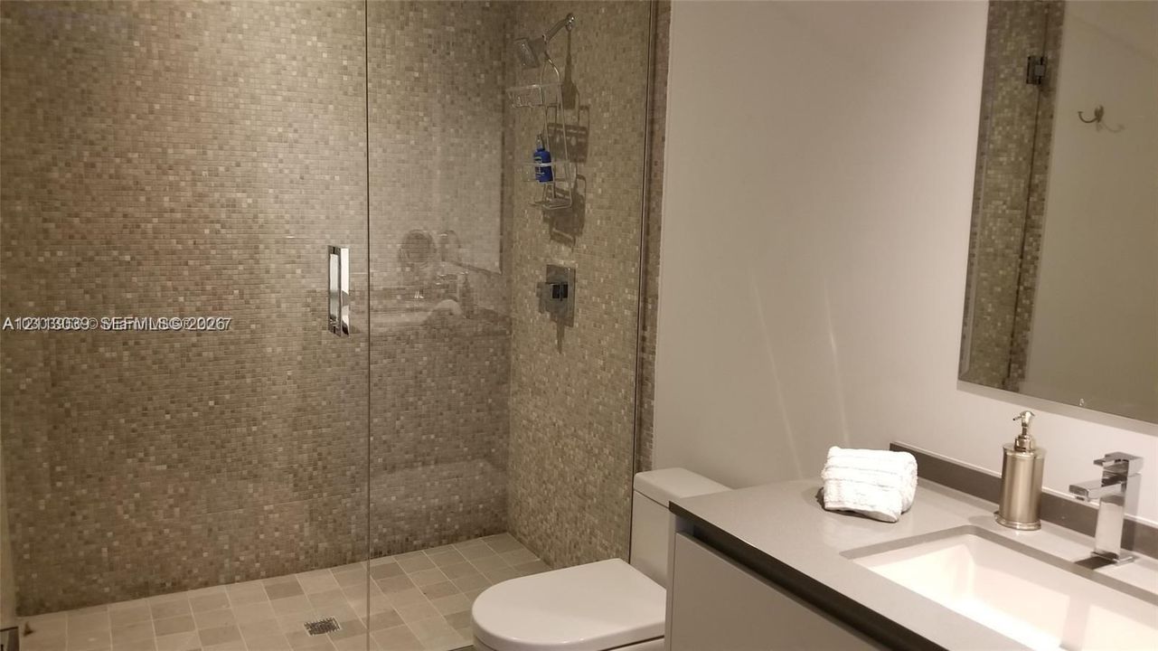 Walk-in shower featuring a glass enclosure and tiled surround, flat-panel vanity with a solid-surface countertop, rectangular undermount sink, and wall-mounted vanity mirror