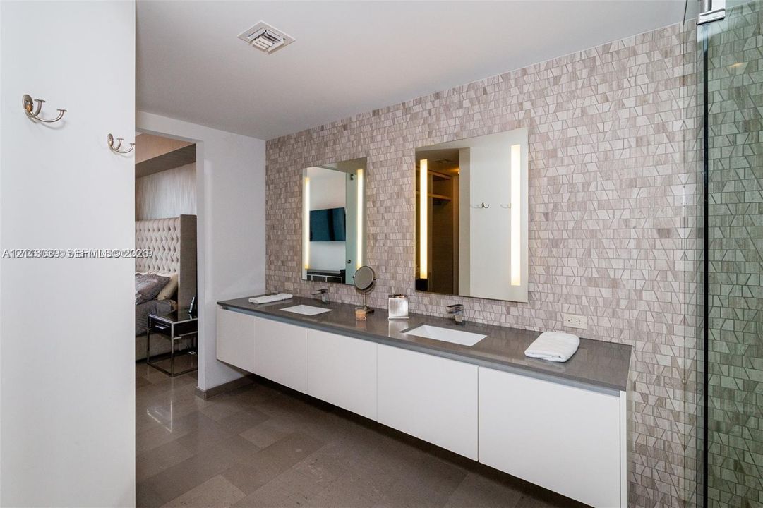Floating dual-sink vanity with a solid surface countertop, mosaic tile backsplash, integrated rectangular sinks, and wall-mounted mirrors with built-in vertical lighting