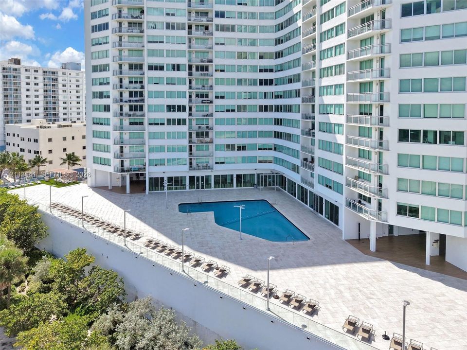 High-rise exterior featuring a paved pool deck, custom-shaped swimming pool, glass balcony railings, and exterior accent lighting