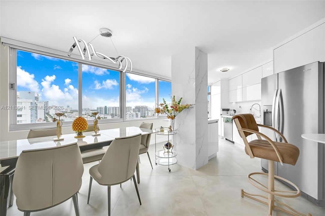 Floor-to-ceiling windows featuring urban scenery, large-format tile flooring, a stone-cladding structural column, custom high-gloss cabinetry, and a contemporary architectural pendant light fixture
