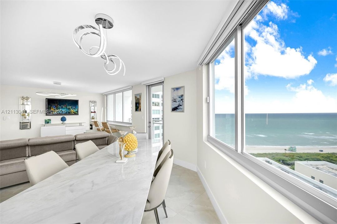 Open-concept living space featuring floor-to-ceiling windows, polished stone flooring, modern LED circular light fixtures, and expansive ocean scenery