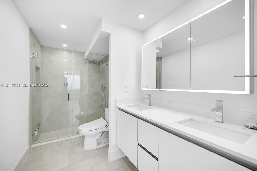 Bathroom featuring a floating double vanity with a stone countertop, integrated LED-lit medicine cabinets, a glass-enclosed walk-in shower with a rainfall showerhead, and tile flooring