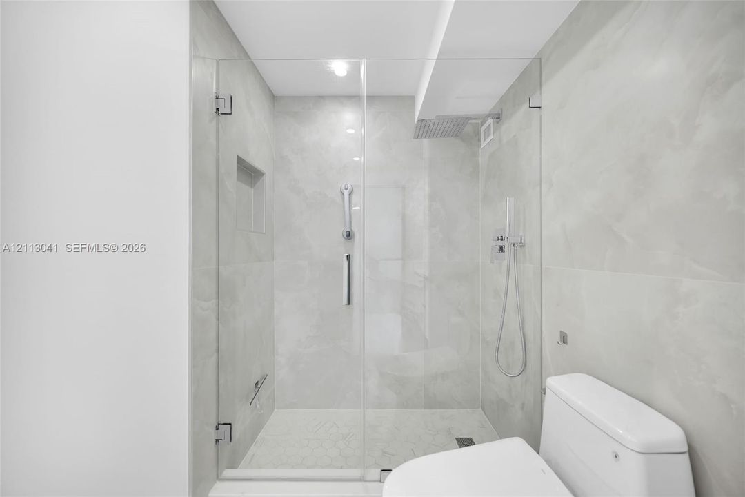 Walk-in shower featuring a frameless glass enclosure, floor-to-ceiling large-format tile surround, integrated shower niche, and wall-mounted shower system