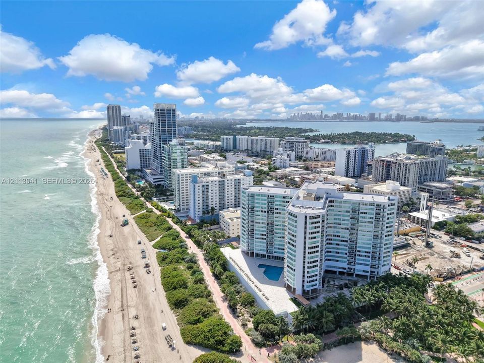 Aerial coastal perspective featuring a multi-story residential building with an attached ground-level swimming pool, situated on a beachfront parcel with direct shoreline access and surrounding palm landscaping