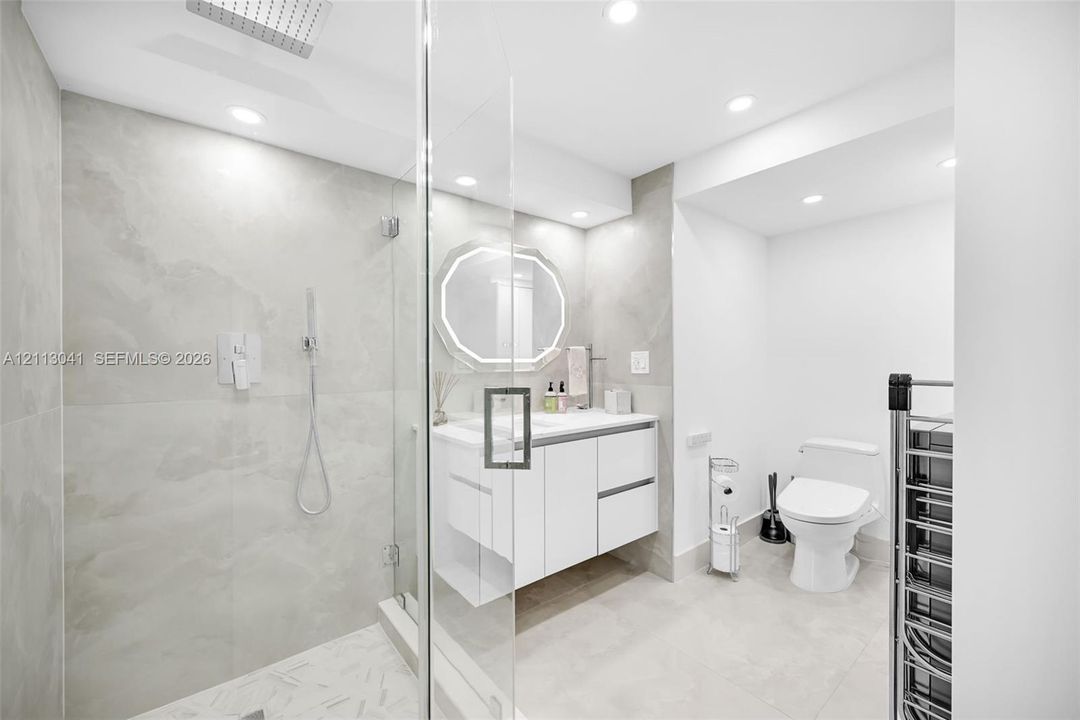 Walk-in shower with floor-to-ceiling stone-finish tile, rainfall shower head, glass enclosure, floating vanity, and recessed lighting