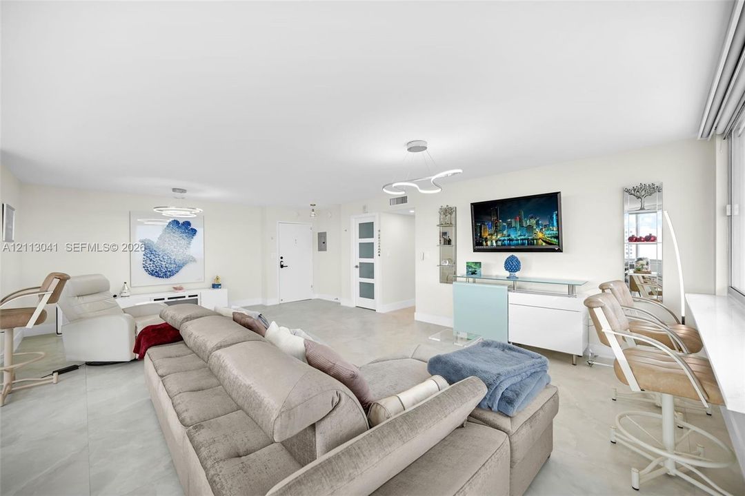 Open-concept living space featuring large-format tile flooring, recessed lighting, modern sculptural light fixtures, and a glass-paneled interior door