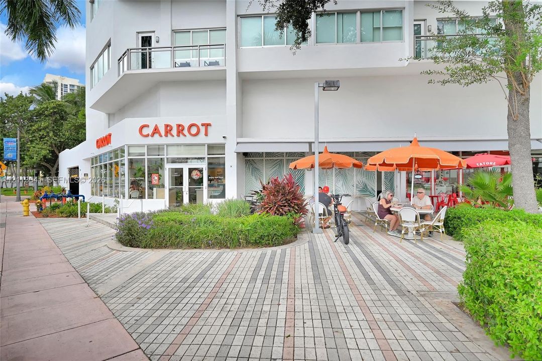Multi-story commercial building exterior featuring expansive floor-to-ceiling storefront windows, integrated ground-level retail space, private balconies, and patterned paver hardscaping