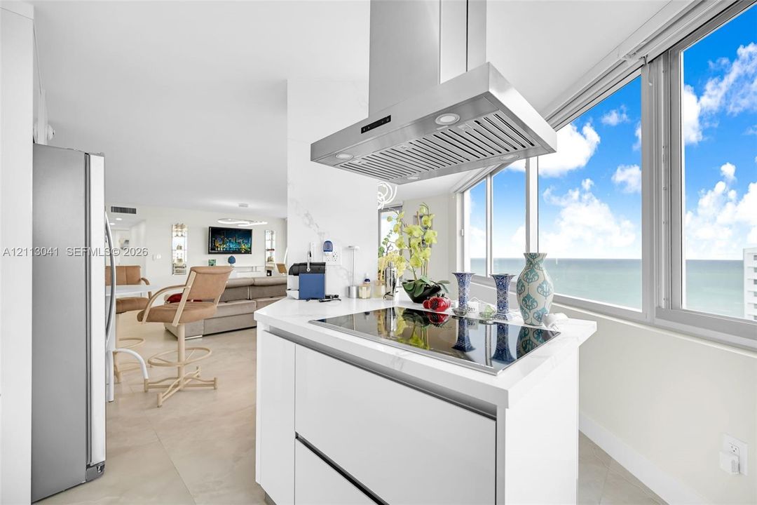 Kitchen featuring white cabinetry, solid-surface countertop, stainless steel range hood, built-in cooktop, and floor-to-ceiling windows
